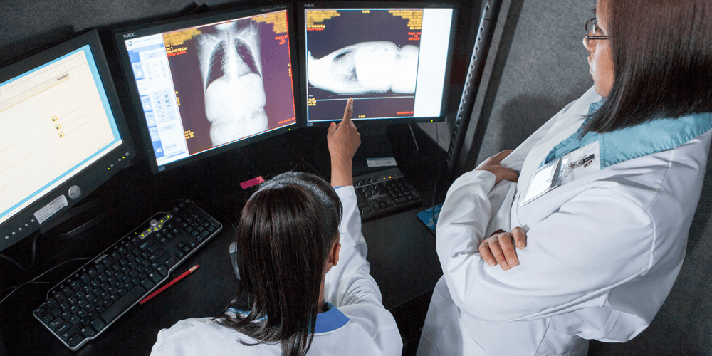 Two female doctors reviewing and analyzing X-ray images together in a clinical setting.