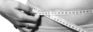 Woman measuring her waist with a tape measure to assess visceral fat.
