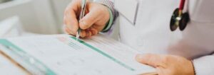 Doctor writing notes in a patient chart during a medical consultation.