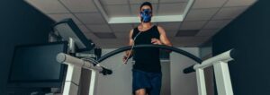 Man wearing a VO2 max testing mask while running on a treadmill, monitored by medical equipment.
